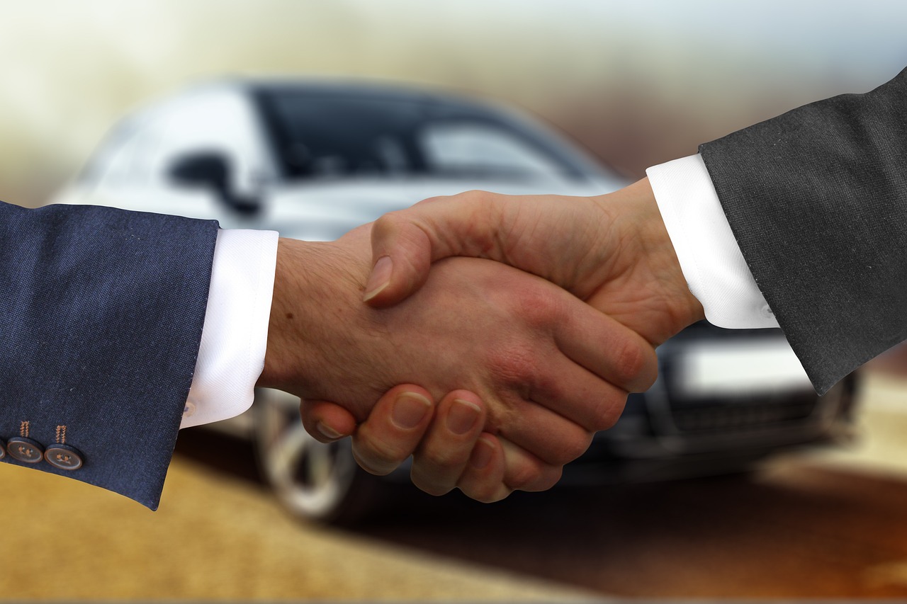 Two people shaking hands in front of a car
