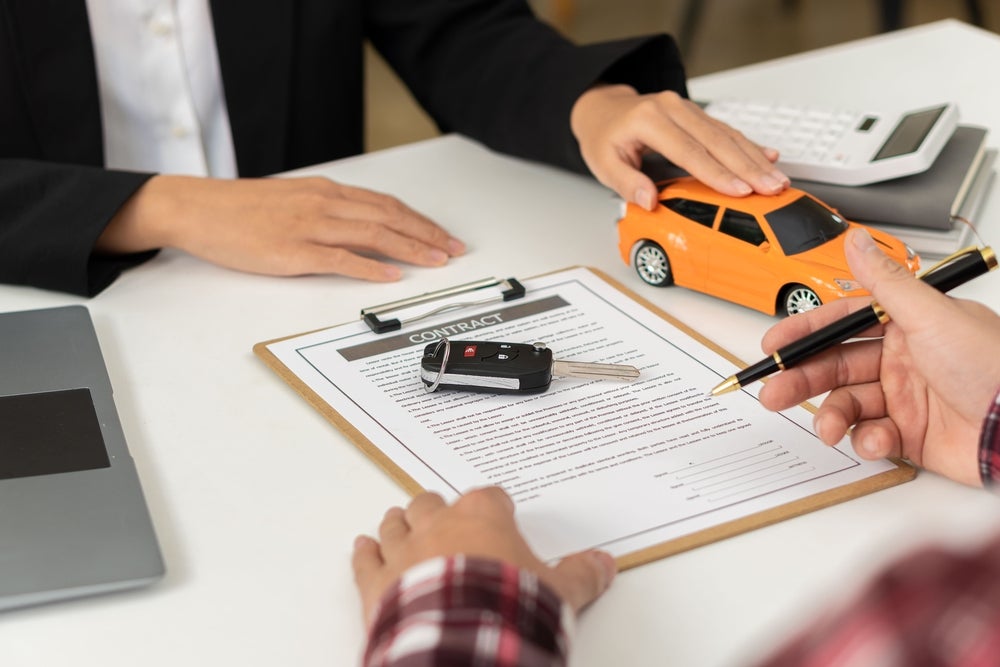 Person signing car title paperwork at a car dealership