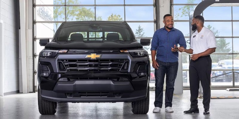 Two men standing in a Chevy service center bay next to a Chevrolet car