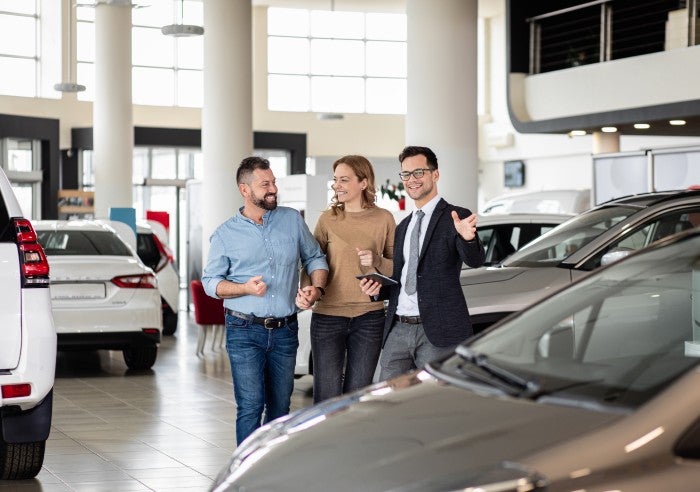Couple and car salesman walking through car dealership showroom
